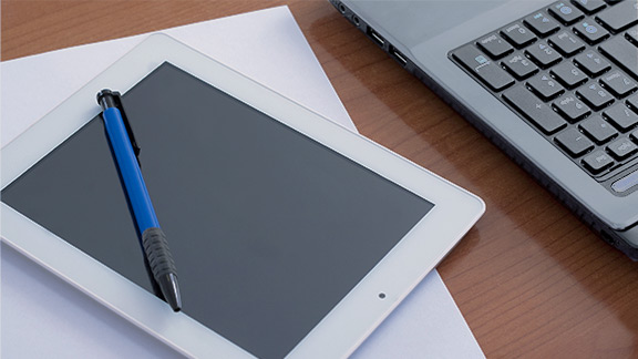 Tablet mit einem Kugelschreiber und Teilansiche einer Laptop Tastatur 