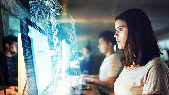 Frau arbeitet mit digitalen Daten am Monitor neben anderen Angestellten.