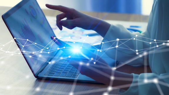 Hands of a woman at a laptop keyboard, in the foreground above the image a string of networked light dots