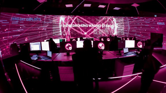 Magenta illuminated control room with warning message on big screen.