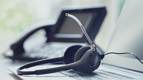 Photo of a headset laying on a laptop with a phone in the background.
