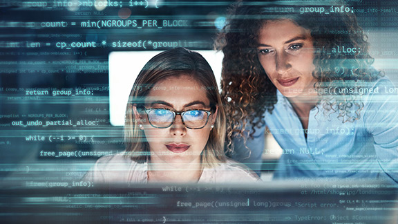 Zwei Frauen vor einem Bildschirm mit Code-Schnipseln im Vordergrund