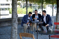 Drei junge Männer arbeiten im Freien an einem Laptop.