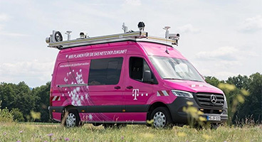 Das T-Surface Car der Telekom fährt auf einer schmalen Straße zwischen Wiesenflächen