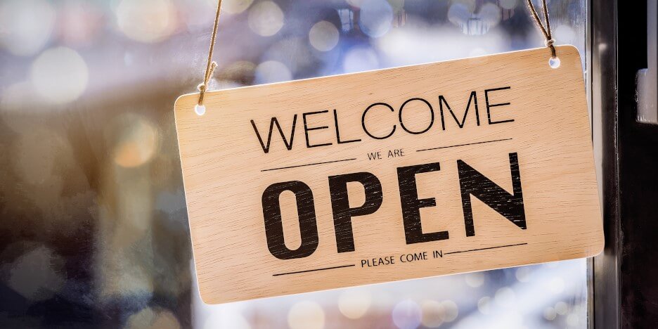 Sign on the glass entrance door with black lettering "Welcome" and "Open" on a light background
