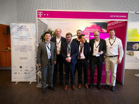Das Telekom Team steht vor dem Telekom Stand auf dem Big Science Business Forum