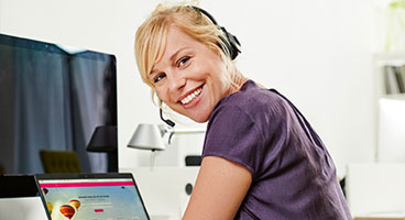 Eine Frau mit Headset vor einem geöffneten Laptop lächelt in die Kamera 