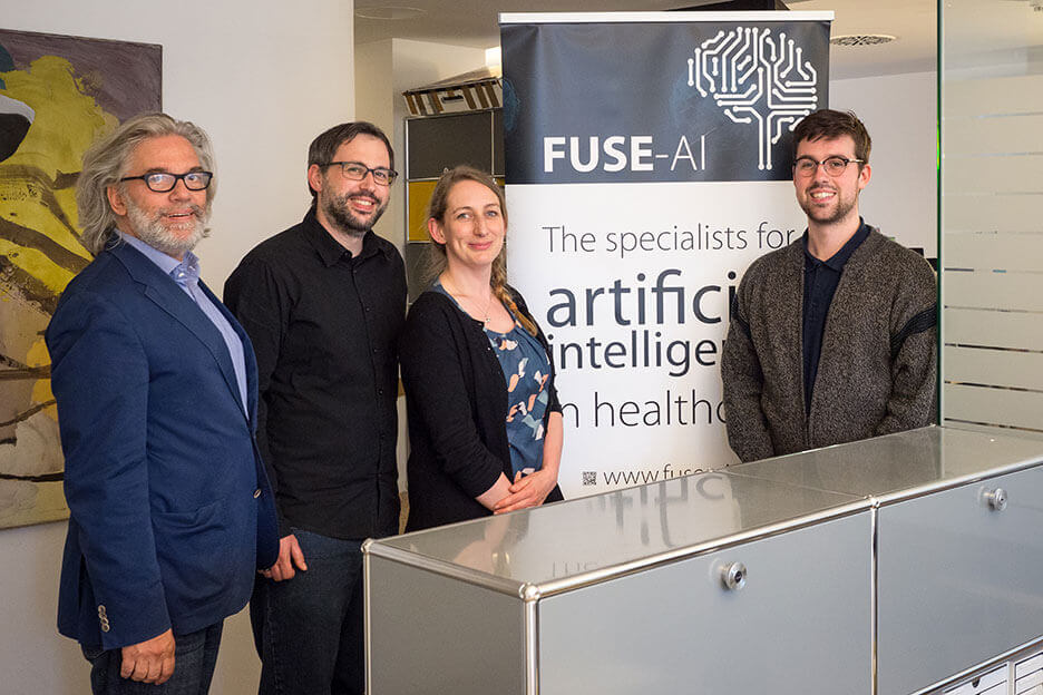 Foto zeigt die Gründer von Fuse-AI im Büro vor einem Aufsteller.