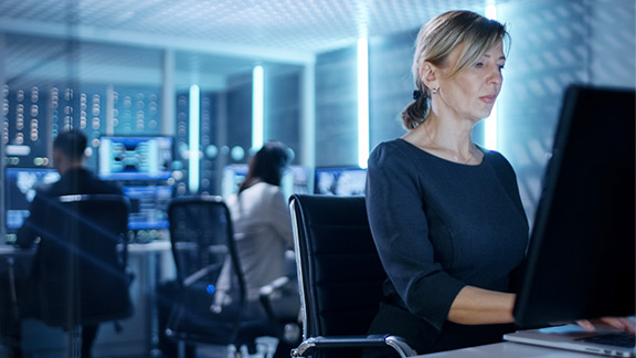 Blond woman sitting at her desk in a control room, working.