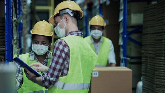 Three workers with protection helmets, face mask and reflective vest working in a store.