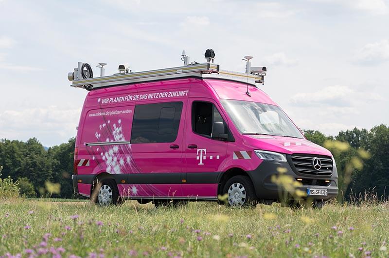 Telekom's T-Surface Car drives along a narrow road between meadows.